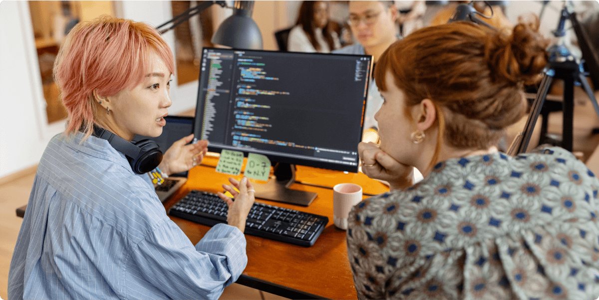 Zwei Frauen diskutieren in einem Büro miteinander über eine Frage im Zusammenhang mit einer Programmierung.