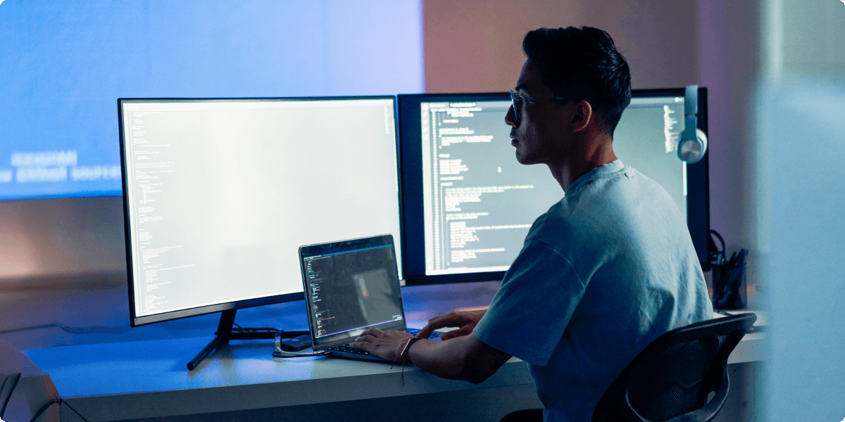 A programmer focused and thinking, lit by the light of his computer screens in his apartment. A projector throws blue ambient light around the room.