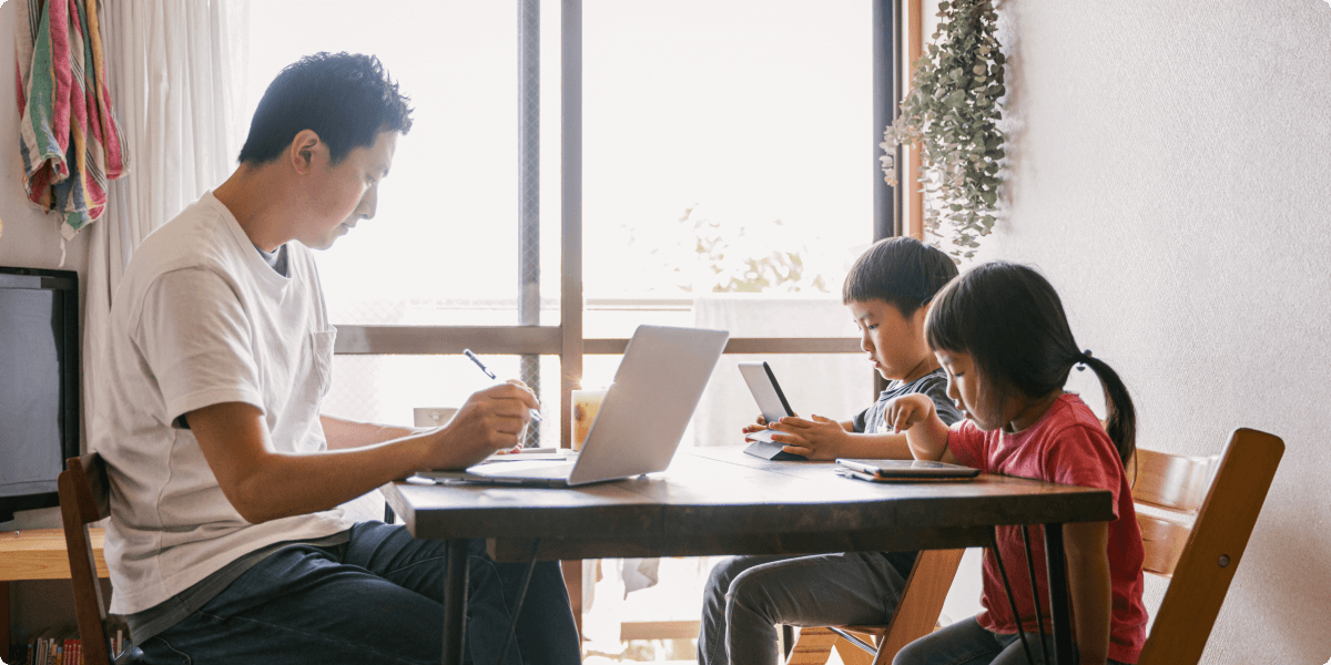 A father at home, studying with his two children at the dining room table.