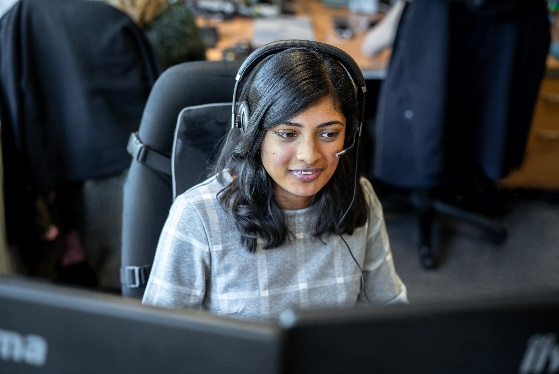 Foto de una mujer con auriculares sentada delante de varios monitores de ordenador.