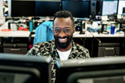 Un hombre sonriendo y mirando dos monitores de equipo.