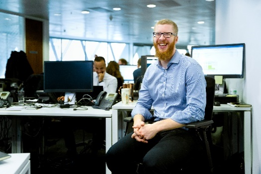 Homme qui sourit à un appareil photo dans un bureau animé.